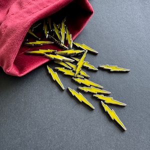 May include: A velvet bag spills out yellow lightning bolt charms. The charms are made of metal with a silver finish and have a yellow enamel coating.