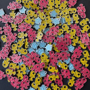 May include: A collection of colorful enamel pins featuring a variety of fish designs. The pins are a mix of red, yellow, and blue, and each fish has a unique eye design. The pins are perfect for adding a touch of whimsy to any outfit or bag.