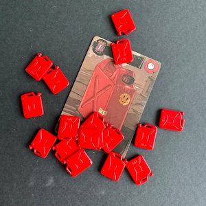 May include: A collection of red plastic toy fuel cans, some with the word "11G" printed on them. The cans are scattered on a gray surface next to a card game with a cartoon image of a fuel can.