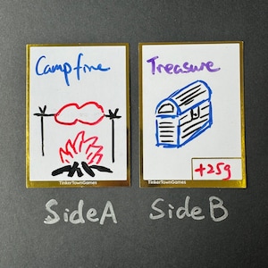 May include: Two illustrated cards with gold borders. The card on the left has a campfire with a red sausage on a stick over the fire. The card on the right has a blue treasure chest with the text "Treasure +259". Both cards have the text "TinkertownGames" at the bottom.