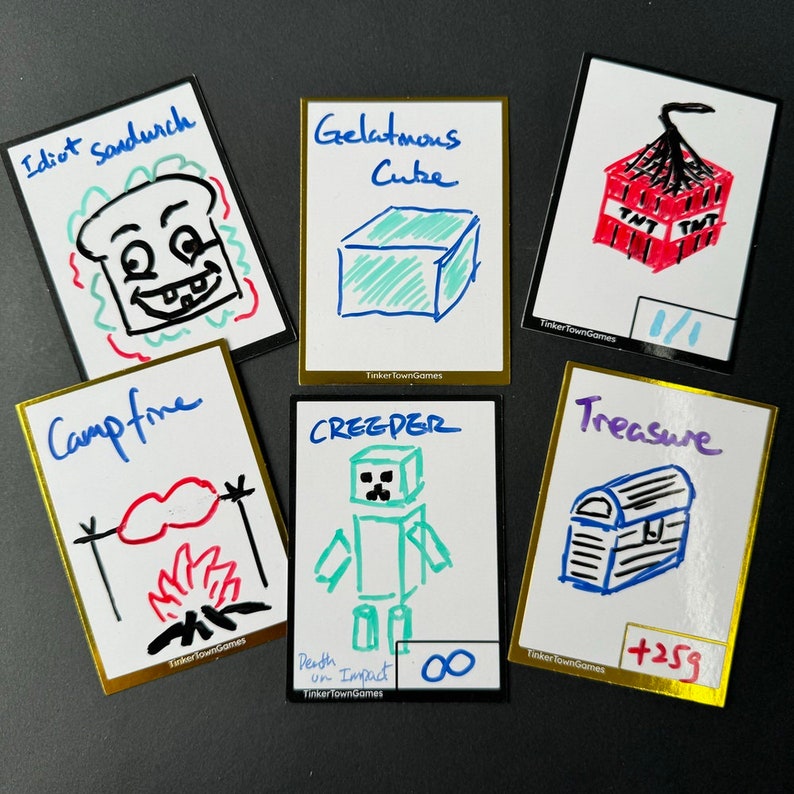 May include: Six illustrated cards with gold borders. The cards feature drawings of a sandwich, a cube, a TNT block, a campfire, a creeper, and a treasure chest. The cards have handwritten text, including "Idiot Sandurch", "Gelatmons Cube", "TNT", "Campfire", "CREEDER", "Treasure", "Death un Impact 00", and "+259".