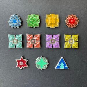 May include: Twelve enamel pins featuring a variety of geometric designs. The pins are in different colours, including blue, green, yellow, red, purple, and orange. The pins are all approximately 2.5 cm in diameter.