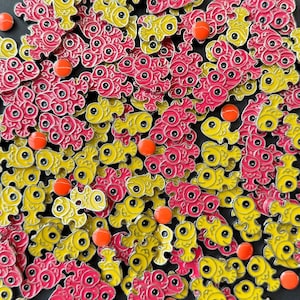 Könnte beinhalten: Eine Nahaufnahme einer großen Sammlung von bunten Emaille-Anstecknadeln in Fischform. Die Fische sind in zwei Farben: Gelb und Pink. Die Anstecknadeln sind in einem zufälligen Muster angeordnet und alle in die gleiche Richtung ausgerichtet.