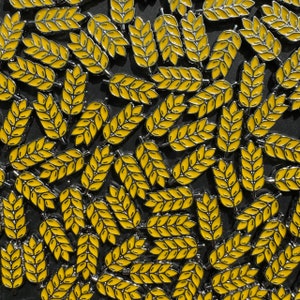 Puede incluir: Una imagen de primer plano de una colección de alfileres de metal dorado con forma de espigas de trigo. Las espigas de trigo son amarillas y tienen un acabado brillante.