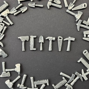 Puede incluir: Primer plano de una superficie negra con una variedad de herramientas en miniatura plateadas dispuestas en círculo alrededor de la palabra "TIT" deletreada con las herramientas.