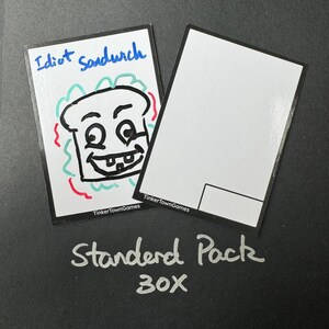 May include: A white card with a black and white drawing of a smiling sandwich with the text "Idiot Sandwich" and the text "TinkerTownGames". A second white card with the text "TinkerTownGames" and the text "Standard Pack 30X" is below the first card.