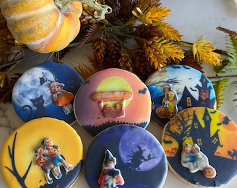 May include: Six Halloween-themed sugar cookies decorated with images of children, a black cat, a witch, a hot air balloon, and a haunted house. The cookies are arranged on a white surface.