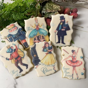 May include: Six decorated sugar cookies featuring characters from the Nutcracker ballet. The cookies are decorated with images of Clara, the Sugar Plum Fairy, the Mouse King, Mother Ginger, Drosselmeyer, and the Nutcracker.