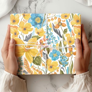 May include: A white gift box with a floral pattern in shades of yellow, blue, and green. The box is tied with a white ribbon.