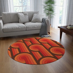 May include: A round, brown, orange, and red area rug with a geometric pattern of curved lines. The rug is in a living room setting with a couch and a plant.