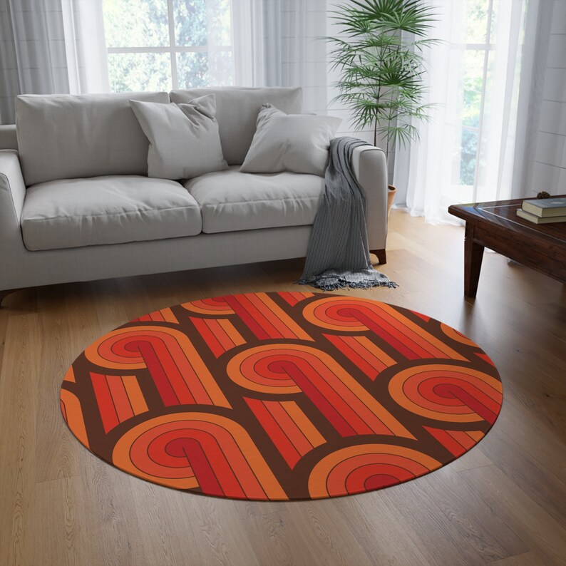May include: A round, brown, orange, and red area rug with a geometric pattern of curved lines. The rug is in a living room setting with a couch and a plant.