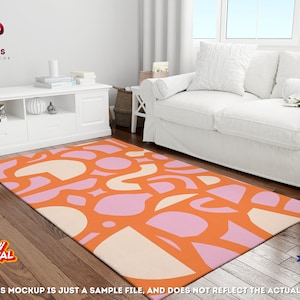Op de afbeelding: Een modern abstract vloerkleed met een geometrisch patroon in tinten oranje, roze en cr&egrave;me. Het vloerkleed ligt op een houten vloer in een woonkamer.