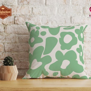 May include: A green and white throw pillow with a floral pattern. The pillow is on a wooden surface in front of a white brick wall.