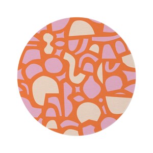 Op de afbeelding: Een rond oranje kleed met een patroon van roze en cr&egrave;mekleurige abstracte vormen.