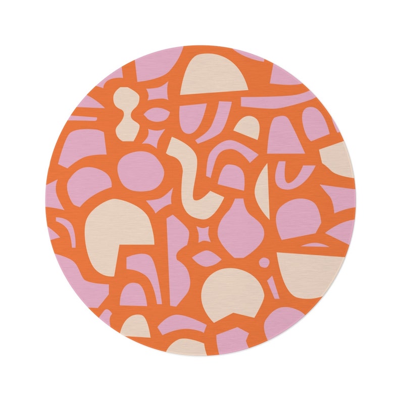 Op de afbeelding: Een rond oranje kleed met een patroon van roze en cr&egrave;mekleurige abstracte vormen.