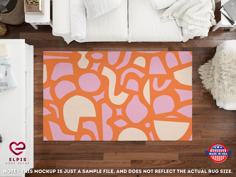 Op de afbeelding: Abstract vloerkleed met een geometrisch patroon in oranje, roze en cr&egrave;me. Het vloerkleed wordt getoond op een houten vloer met een witte bank en een pluche wit vloerkleed op de achtergrond.