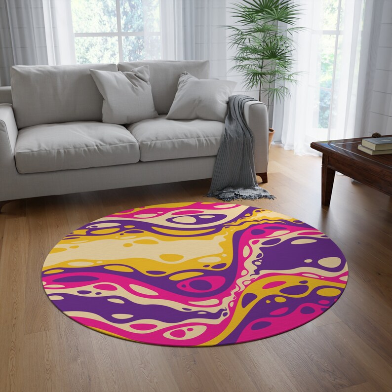 May include: A round rug with a colorful abstract design. The rug features a swirling pattern of yellow, pink, and purple.