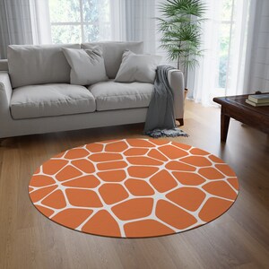 May include: A round orange and white patterned area rug with a geometric design. The rug is on a hardwood floor in a living room setting.