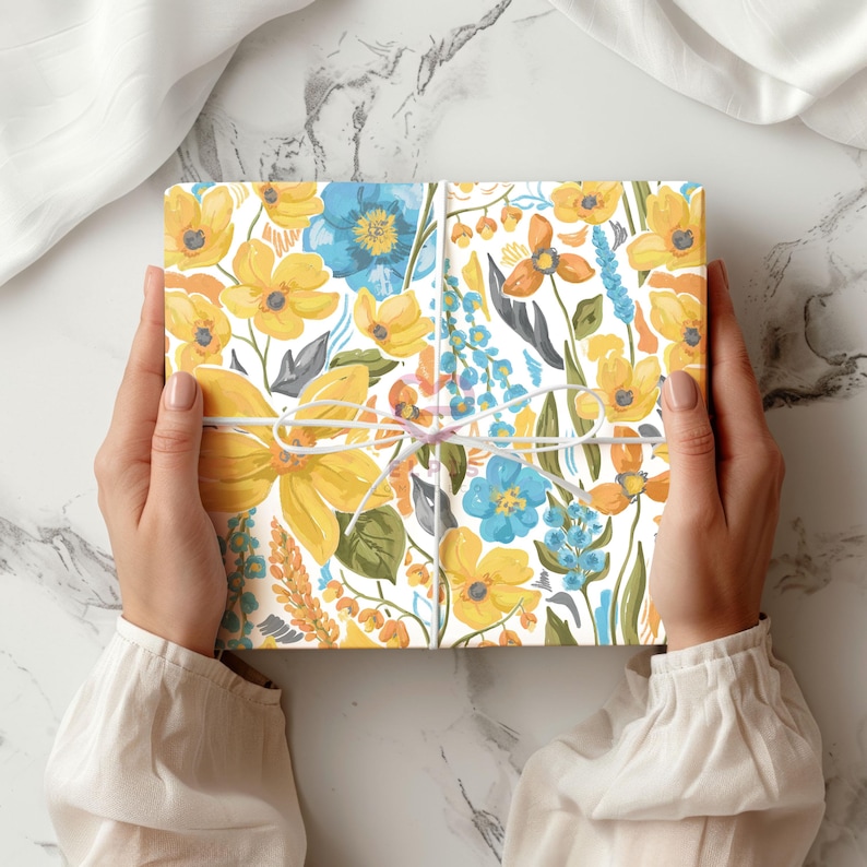 May include: A white gift box with a floral pattern in shades of yellow, blue, and green. The box is tied with a white ribbon.