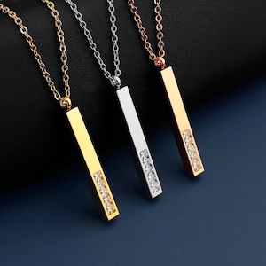Puede incluir: Tres collares con colgantes de barra adornados con piedras de circonita cúbica transparentes. Los collares son de oro, plata y oro rosa.
