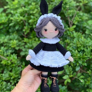 Puede incluir: Una muñeca de crochet vestida con un traje de criada blanco y negro con orejas de conejo. La muñeca tiene el pelo gris y botas negras.