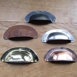 Può includere: Cinque tiretti per cassetti in metallo in diverse finiture. I tiretti sono tutti a forma di semicerchio e hanno una leggera curvatura al centro. Le finiture includono nero, ruggine, argento, oro e rame.