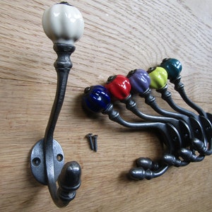 May include: Set of six cast iron hooks with ceramic knobs in various colors, including blue, red, purple, yellow, and green. The hooks are mounted on a wooden surface.