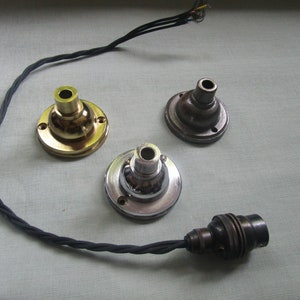 May include: Three different types of light fixture ceiling mounts with a black electrical cord. The mounts are gold, silver, and bronze.