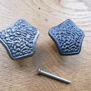 May include: Two decorative cabinet knobs with a textured, star-shaped design. One knob is silver and the other is black. A silver screw is included.