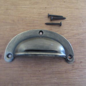 Può includere: Maniglia a coppa in ottone anticato con tre viti scure. La maniglia a forma di mezzaluna ha due fori per le viti su ciascuna estremità e uno al centro. L'hardware è progettato per armadi, cassetti o altri mobili.