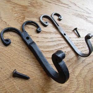 May include: Two black metal hooks with decorative swirls. The hooks are attached to a wooden surface with screws.