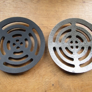 Op de afbeelding: Twee ronde metalen afvoerdeksels, een zwart en een zilver, met een concentrisch cirkelontwerp.