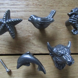May include: Six different metal drawer pulls in the shape of a starfish, bird, seahorse, dolphin, and buffalo. The pulls are all a dark gray color.