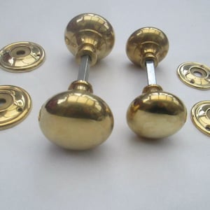 Könnte beinhalten: Zwei Sätze polierter Messing-Türknäufe mit runden Rosetten. Jeder Knauf hat eine runde, gewölbte Form und ein schlichtes, elegantes Design.