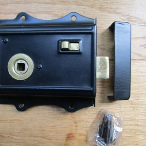 May include: Black door latch with a brass keyhole and a brass latch. The latch is attached to a wooden surface with screws.
