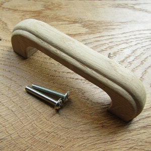 May include: A wooden cabinet handle with a rounded, curved design. The handle is light brown in colour and comes with two silver screws.