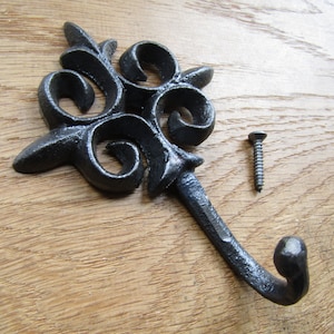 May include: Black cast iron hook with a decorative scroll design. The hook is attached to a wooden surface with a screw.