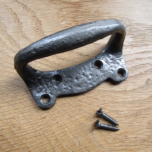 Puede incluir: Pomo de puerta de hierro fundido negro con acabado rústico. El pomo tiene la parte superior redondeada y dos agujeros de montaje a cada lado. Se incluyen dos tornillos.