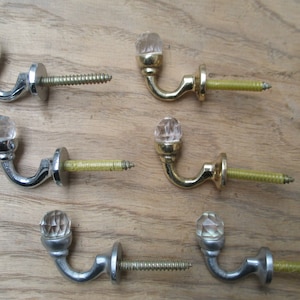 May include: Six decorative hooks with crystal finials. Three hooks are silver and three are gold. Each hook has a screw for mounting.