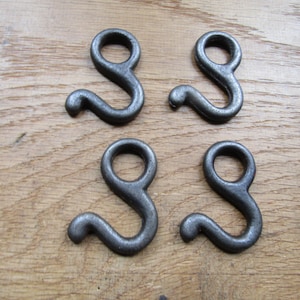 Könnte beinhalten: Vier silberne Metallhaken mit einer Schlaufe oben und einem gebogenen Haken unten. Die Haken sind in zwei Reihen zu je zwei auf einer Holzoberfläche angeordnet.