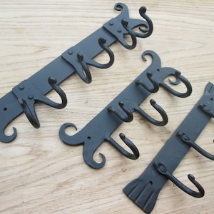 May include: Three black metal wall mounted hooks with decorative scrollwork. Each hook has multiple hooks for hanging items.