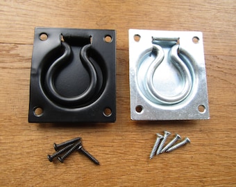Op de afbeelding: Twee vierkante metalen ringgrepen, een zwart en een zilver, met vier schroeven per stuk.