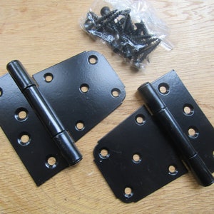 Puede incluir: Dos bisagras de puerta de metal negro con un paquete de tornillos. Las bisagras tienen cinco agujeros a cada lado y un barril redondo en el medio.