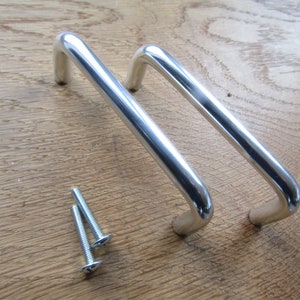 May include: Two silver metal cabinet door handles with rounded edges and a simple design. The handles are shown with three silver screws.