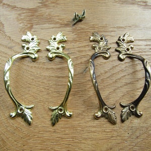 Könnte beinhalten: Vier verzierte Metall-Schubladengriffe mit einem Blattdesign. Zwei sind golden und zwei sind schwarz.