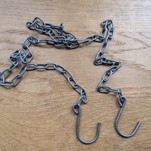 May include: A silver chain with two hooks at the ends. The chain is lying on a wooden surface.