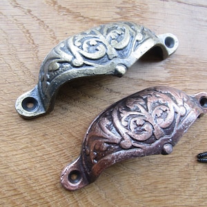 Puede incluir: Dos tiradores de cajón de hierro fundido ornamentados con un diseño floral. Un tirador es dorado y el otro es de cobre.