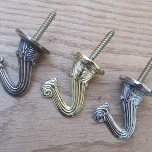 Può includere: Tre ganci in metallo decorati con un motivo a volute. I ganci sono rifiniti in argento, oro e ottone.