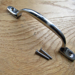 May include: A chrome door handle with a curved design and two screws. The handle is on a wooden surface.