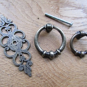 Puede incluir: Tres tiradores de armario de estilo antiguo en acabado latón. Un tirador es una placa decorativa con un diseño floral. Los otros dos tiradores son en forma de anillo con un borde de cuentas.